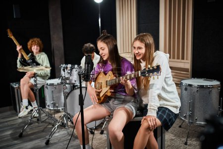 Foto de Se centran en las adolescentes con el canto de la guitarra con amigos borrosos con batería y guitarra en el telón de fondo - Imagen libre de derechos