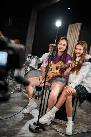 Foto de Alegre adorable adolescentes cantando y tocando varios instrumentos en estudio, grupo musical - Imagen libre de derechos