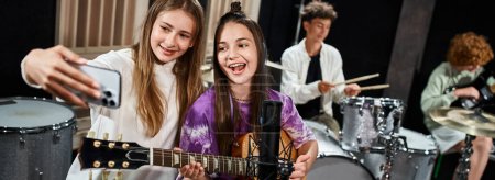 Photo for Focus on happy teens taking selfie with blurred friends playing instruments on backdrop, banner - Royalty Free Image