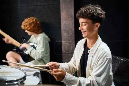 Photo for Focus on adorable teenage boy with braces playing drums next to his blurred friend with guitar - Royalty Free Image