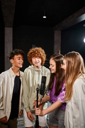 Foto de Alegre talentoso adolescentes y niñas cantando juntos y sonriendo en el estudio, grupo musical - Imagen libre de derechos