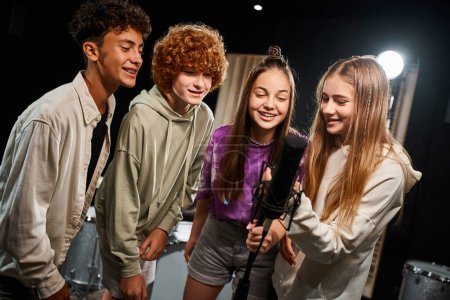 Photo for Cheerful cute teenagers in everyday vibrant attires singing together into microphone, musical group - Royalty Free Image
