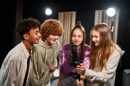 Foto de Cuatro adolescentes talentosos alegres en trajes casuales cantando juntos mientras están en el estudio, grupo musical - Imagen libre de derechos