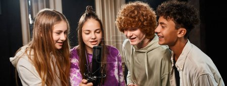 Foto de Alegres adolescentes talentosos con atuendos casuales cantando juntos en estudio, grupo musical, pancarta - Imagen libre de derechos