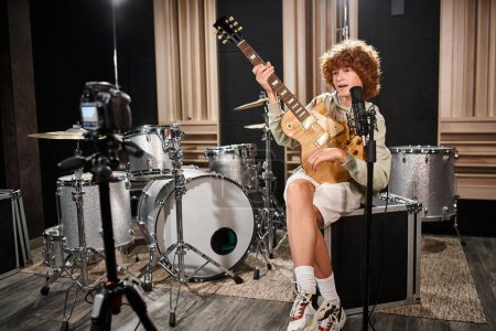 Foto de Bien parecido pelirrojo adolescente tocando su guitarra y cantando canción en el micrófono en el estudio - Imagen libre de derechos