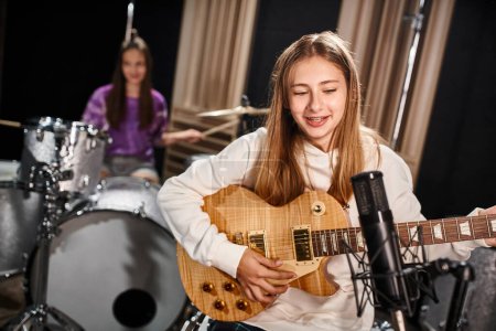 Photo for Focus on pretty teenage girl playing guitar and singing next to her blurred friend playing drums - Royalty Free Image