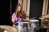 good looking brunette teenage girl in vibrant casual attire playing drums while in music studio Stickers #687124490