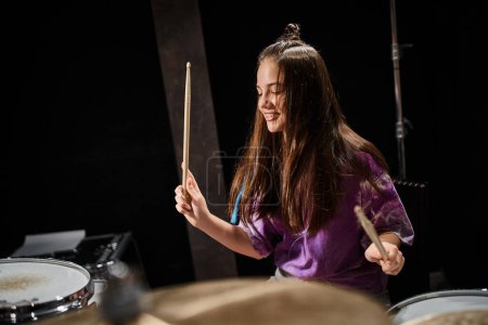 freudig gut aussehende talentierte brünette Teenagerin mit langen Haaren, die im Studio Schlagzeug spielt