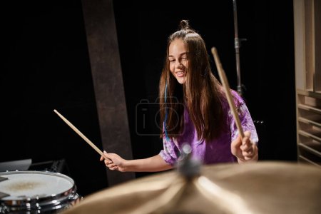 cheerful talented adorable teenage girl in everyday bold outfit playing drums while in studio