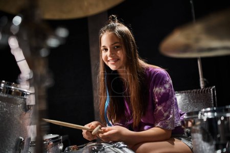 Foto de Adorable alegre adolescente en vibrante atuendo tocando su batería y sonriendo felizmente a la cámara - Imagen libre de derechos