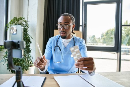 doctor afroamericano guapo enfocado sosteniendo píldoras y tomando notas mientras que consulta por teléfono