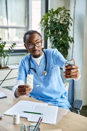 médecin afro-américain concentré consultant patient par téléphone et tenant des pilules, télémédecine