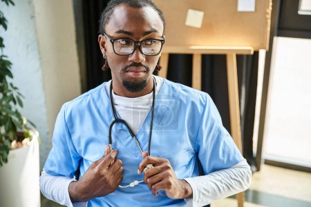 nachdenklich gut aussehender afrikanisch-amerikanischer Arzt mit Brille, Stethoskop haltend und wegschauend