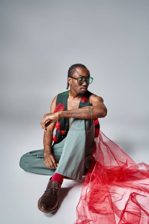 hombre afroamericano guapo con tela de tul rojo en su chaleco sentado en el suelo, concepto de moda