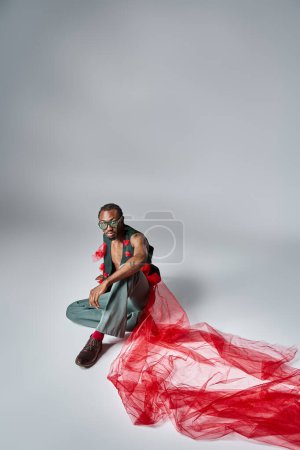 handsome african american male model with sunglasses in fashionable attire sitting on floor