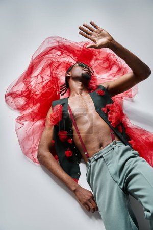 Téléchargez les photos : Bel homme afro-américain à la mode avec des lunettes de soleil en tenue tendance couché sur le sol, la mode - en image libre de droit