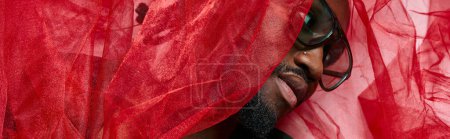 portrait de jeune homme afro-américain avec du tissu de tulle rouge couché sur le sol, concept de mode, bannière
