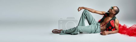 Téléchargez les photos : Bel homme afro-américain en tenue élégante avec tissu en tulle rouge inclinable sur le sol, bannière - en image libre de droit
