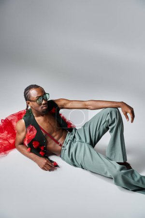Téléchargez les photos : Beau homme afro-américain en tenue à la mode avec tissu en tulle rouge inclinable sur le sol - en image libre de droit