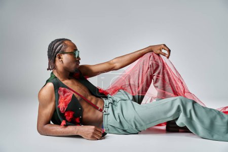 appealing african american man in fashionable attire with red tulle fabric reclining on floor
