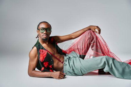 Téléchargez les photos : Bel homme afro-américain en tenue à la mode avec un tissu en tulle rouge inclinable sur le sol - en image libre de droit