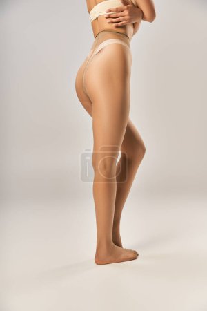 cropped view of woman in seamless tights and beige underwear posing on grey background