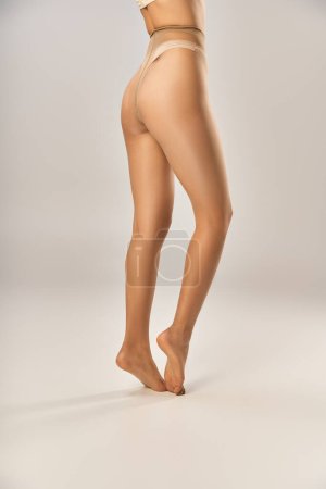 partial view of young woman in seamless pantyhose and beige underwear posing on grey background