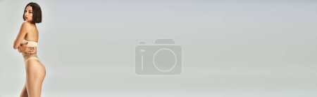 Téléchargez les photos : Bannière de jeune femme asiatique en collants sans couture et sous-vêtements beige posant sur fond gris - en image libre de droit