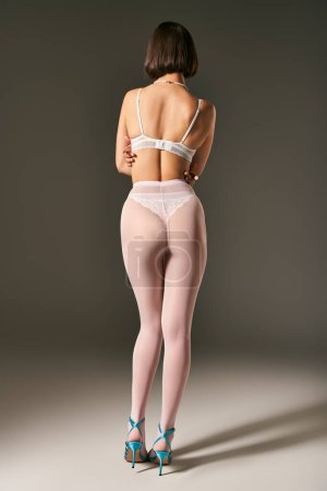 back view of woman with short hair posing in pantyhose and bra on grey background, hosiery