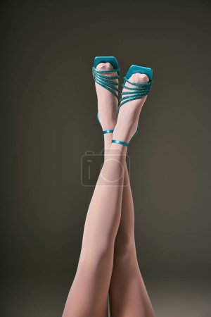 elegant female crossed legs in white pantyhose and blue shoes on grey background, hosiery
