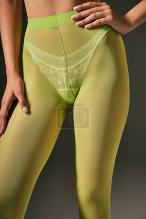 cropped young woman in green tights posing with hand on hip on grey background, hosiery concept