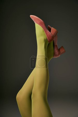 vista recortada de mujer joven en medias de nylon verde acostado sobre fondo gris oscuro, concepto de calcetería