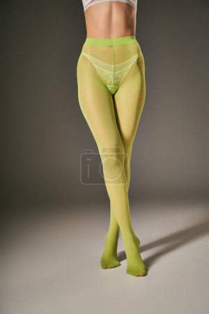 Ausgeschnittene Ansicht einer jungen Frau in grünen Nylonstrumpfhosen, die auf dunkelgrauem Hintergrund posiert, gekreuzte Beine