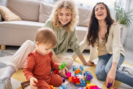 cheerful beautiful lesbian couple playing with their toddler daughter at home, modern parenting