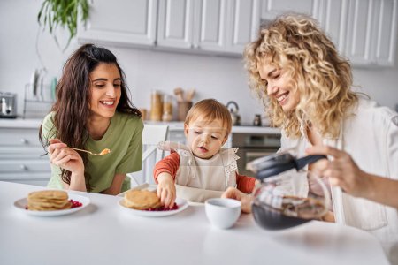 Téléchargez les photos : Heureux attrayant couple lgbt avoir délicieux petit déjeuner avec leur petite fille, concept de famille - en image libre de droit