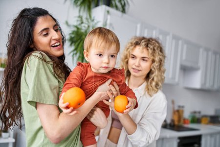 Téléchargez les photos : Joliment joli couple lgbt s'amuser avec leur jolie petite fille tenant des mandarines, famille - en image libre de droit