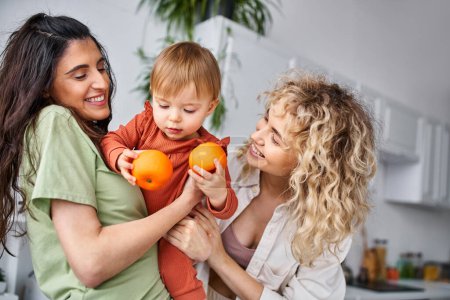 Téléchargez les photos : Amour couple lgbt s'amuser avec leur mignon bébé fille tenant des mandarines, concept de famille - en image libre de droit