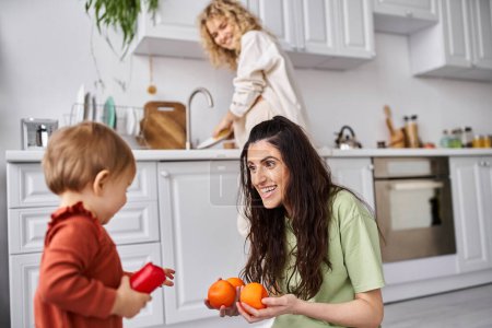 Téléchargez les photos : Se concentrer sur la femme heureuse avec sa fille tenant des mandarines avec son partenaire blond flou sur toile de fond - en image libre de droit
