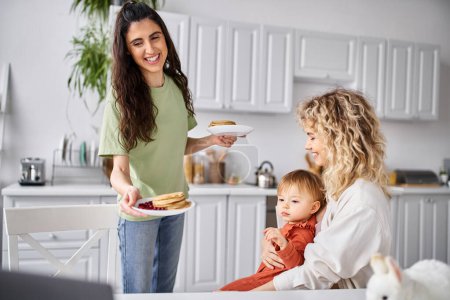 Téléchargez les photos : Beau joyeux couple lesbien avoir pancakes sur le petit déjeuner avec leur bébé fille, concept de famille - en image libre de droit