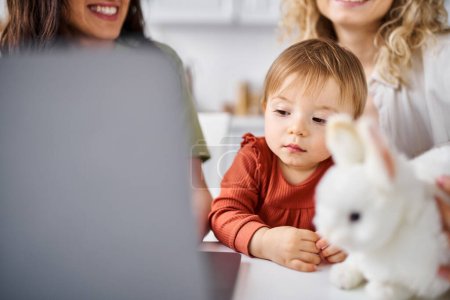 charmantes lesbisches Paar in Homewear, das mit seinem kleinen Mädchen auf dem Laptop Filme anschaut, Familienkonzept