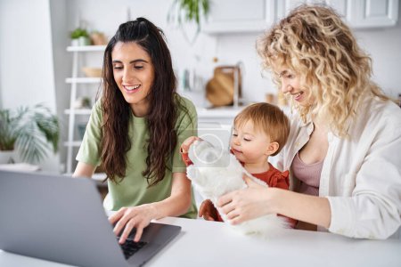 nährendes lesbisches Paar in Homewear, das mit seinem kleinen Mädchen auf dem Laptop Filme anschaut, Familienkonzept