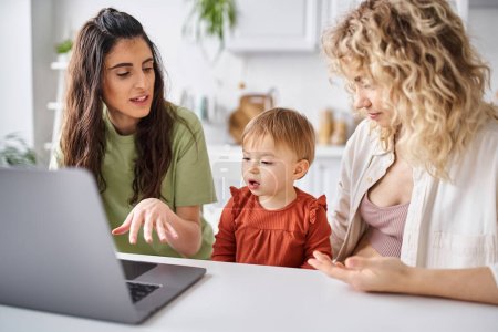 loving lgbt couple watching movies with their daughter on laptop on kitchen, modern parenting