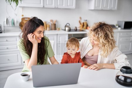 caring lgbt couple watching movies with their daughter on laptop on kitchen, modern parenting