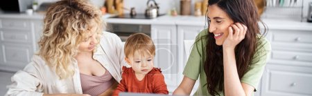 joyous lgbt couple watching movies with their daughter on laptop on kitchen, modern parenting