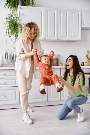 attractive cheerful lesbian couple playing actively with their toddler daughter, modern parenting