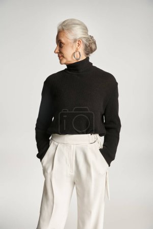 portrait of middle aged business woman in elegant attire posing with hands in pockets on grey