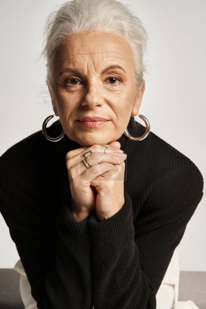 business portrait, middle aged business woman in turtleneck looking at camera on grey backdrop
