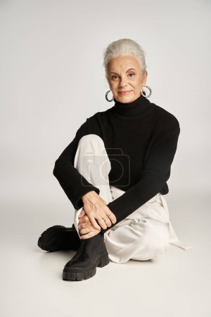 mujer de negocios feliz de mediana edad en elegante atuendo casual elegante sentado sobre fondo gris