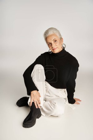 glückliche Geschäftsfrau mittleren Alters in eleganter schicker Freizeitkleidung sitzt auf grauem Hintergrund