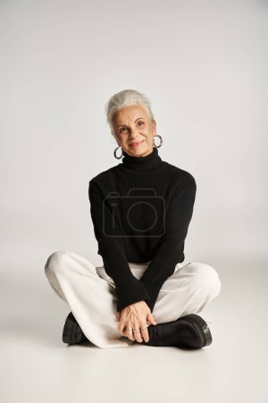 cheerful middle aged business woman in elegant smart casual attire sitting on grey background
